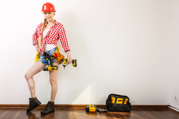 Woman wearing helmet using drill. Girl working at flat remodeling. Building, repair and renovation. - Foto, Bild