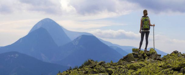 Πίσω όψη του νεαρή λεπτή backpacker τουριστικά κορίτσι με ραβδί στέκεται στην βραχώδη κορυφή ενάντια σε φωτεινό μπλε ουρανό πρωί απολαμβάνοντας ομίχλη οροσειρά Πανόραμα. Τουρισμός, ταξίδια και αναρρίχηση έννοια. - Φωτογραφία, εικόνα