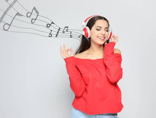 Young woman with headphones and music notes against light background. Space for text - Foto, afbeelding