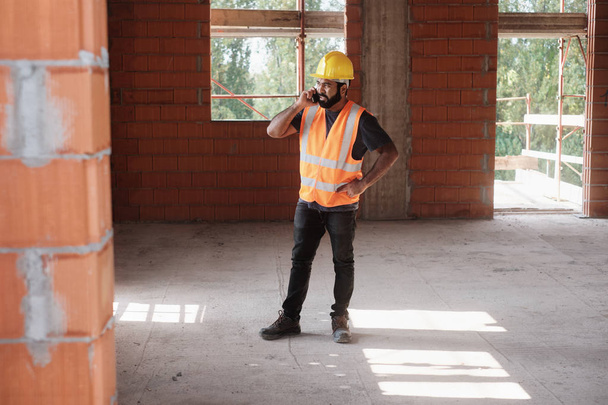 Gülümseyen ve Smartphone kullanarak inşaat alanında çalışan adam - Fotoğraf, Görsel