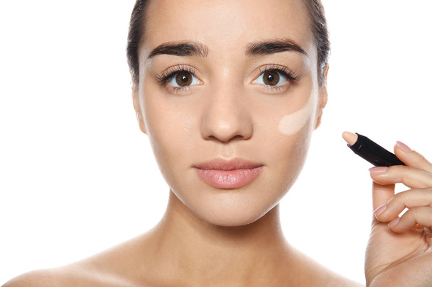 Young woman applying foundation on her face against white background - Valokuva, kuva