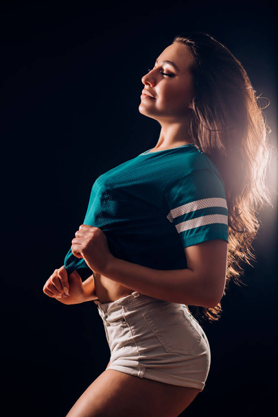 Silhouette portrait of a beautiful brunette woman sideways. Sexy girl in white shorts and t-shirt smiles and closes her eyes. Slim figure, fitness, dancing - 写真・画像