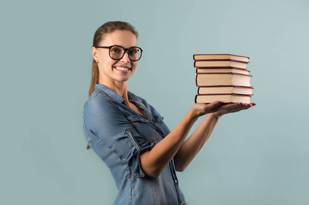 beautiful young girl with glasses holding books in her hands against a blue background - Foto, Imagen