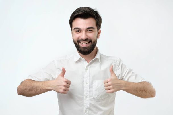 Yeah I like it concept. Pleased and satisfied male in white shirt raising thumbs up - Fotoğraf, Görsel
