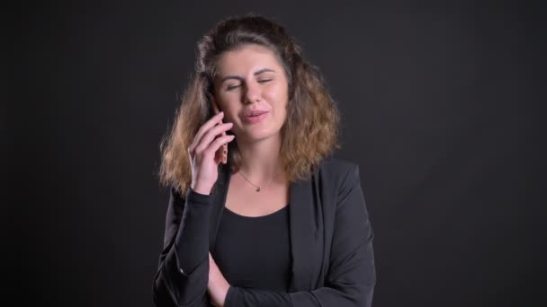 Close-up portrait of overweight caucasian woman smilingly talking on cellphone on black background. - Video