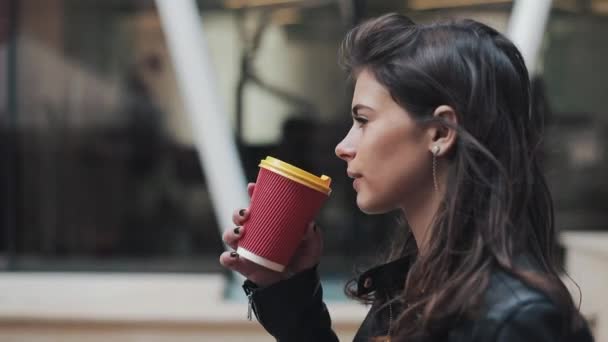 Beautiful young woman with an attractive appearance, adorable look and autumn jacket in the city. Amazing view of business lady with a cup of coffee walking down the city street - Filmagem, Vídeo