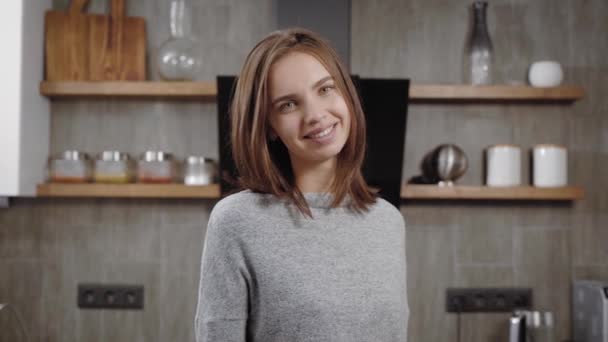 charming young brunette woman is smiling standing in a kitchen in apartment, looking at camera and posing, medium shot portrait - Filmmaterial, Video