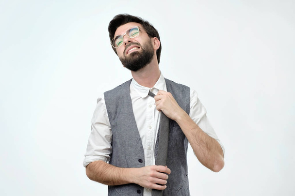 young hispanic man loosing tie on grey background. He is feeling that can not breathe. - Foto, Imagem