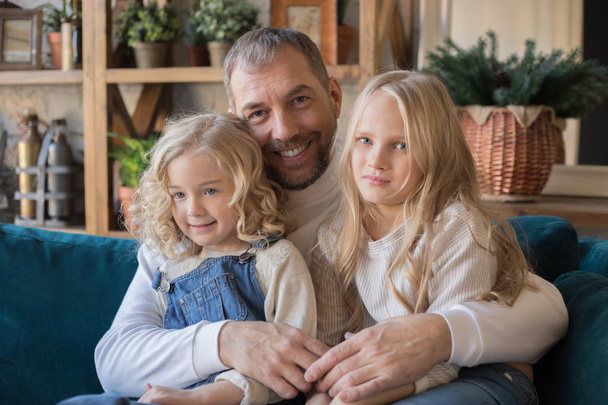 Portrait of a father and two daughters sitting in an embrace. - Foto, afbeelding