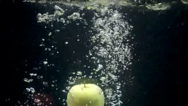 Footage of falling apples in the water on black background - Felvétel, videó