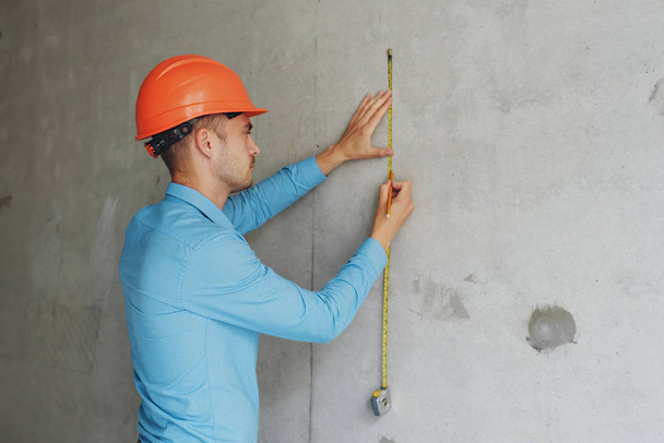 Satisfied construction worker foreman measures a tape measure of a wall parameter in a house under construction. Inspects repair readiness and accuracy of work performed - Φωτογραφία, εικόνα