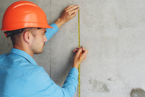 Spokojený stavební dělník mistr měří metr zdi parametru v domě ve výstavbě. Kontroluje připravenost opravit a přesnost provedených prací - Fotografie, Obrázek