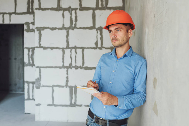 Construction supervisor writes on notebook near the wall. Handsome foreman taking notes in clipboard. Construction inspector checking new object - Foto, imagen