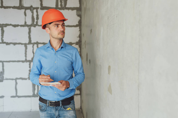 Construction supervisor writes on notebook near the wall. Handsome foreman taking notes in clipboard. Construction inspector checking new object - Foto, Bild