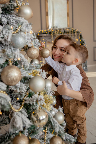 Mother and his little son decorating Christmas tree with toys and garlands. - Fotografie, Obrázek