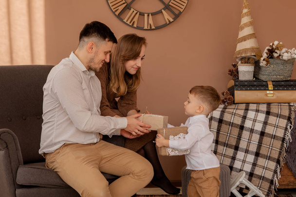 Little boy gives parents a gift box. Birthday gifts . Little son with his family. Holidays, present, childhood, happiness concept. Little boy celebrating birthday with his parents. - Photo, image