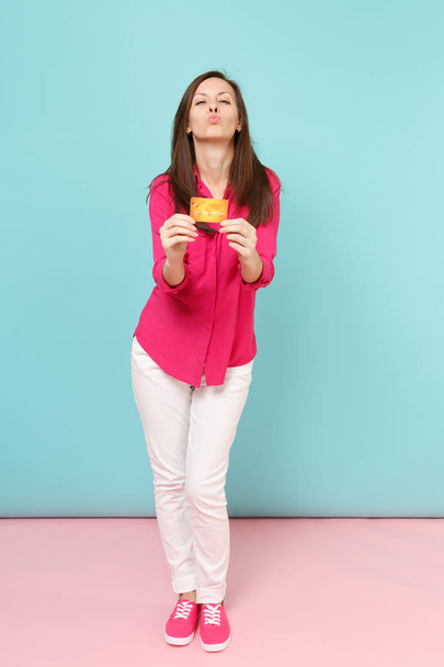 Портрет усміхненої молодої жінки в блузці з трояндової сорочки білі штани тримають кредитну картку ізольовано на яскраво-рожевому синьому пастельному фоні фотостудії. Концепція модного способу життя. Збільшити простір для копіювання
 - Фото, зображення