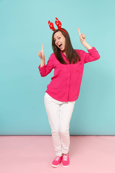 Retrato de larga duración de la divertida mujer joven en camisa rosa blusa, pantalones blancos, cuernos de ciervo posando aislado en brillante rosa azul pastel estudio de fondo de la pared. Concepto de estilo de vida. Simular espacio de copia
 - Foto, Imagen