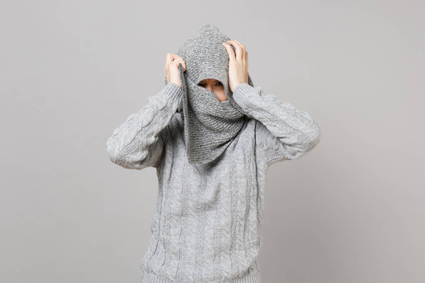スカーフで顔を覆っている灰色のセーター折り返しの若い女性は、灰色の背景上に分離されて頭に手を置きます。健康的なファッションのライフ スタイルの人々 の誠実な感情、寒い季節の概念。コピー スペースをモックアップします。 - 写真・画像