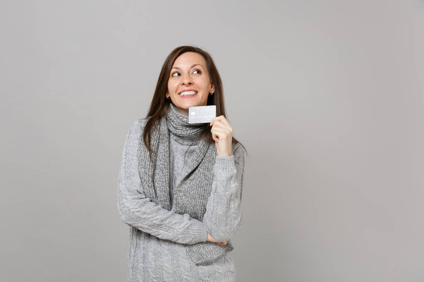 灰色のセーター マフラー探して、灰色の背景に分離された信用銀行カードを保持で溶け込む若い女性。健康的なファッションのライフ スタイルの人々 の誠実な感情、寒い季節の概念。コピー スペースをモックアップします。 - 写真・画像