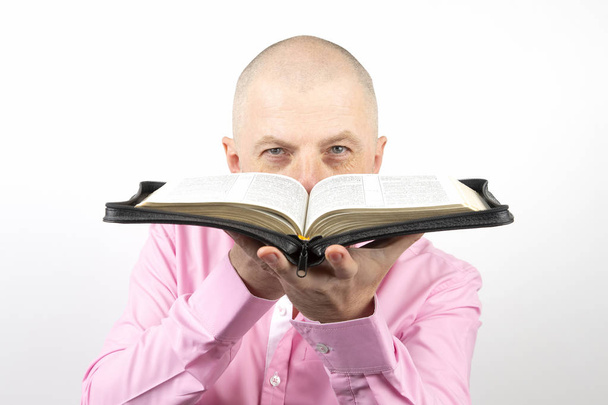vousatý muž v růžové košili vypadá prostřednictvím otevřené Bible - Fotografie, Obrázek