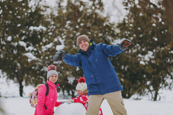 Heureuse femme de famille, homme petite fille en vêtements chauds jeu faire bonhomme de neige, jeter des boules de neige dans un parc enneigé ou la forêt à l'extérieur. Amusement d'hiver, loisirs en vacances. relation amoureuse style de vie familial concept
 - Photo, image