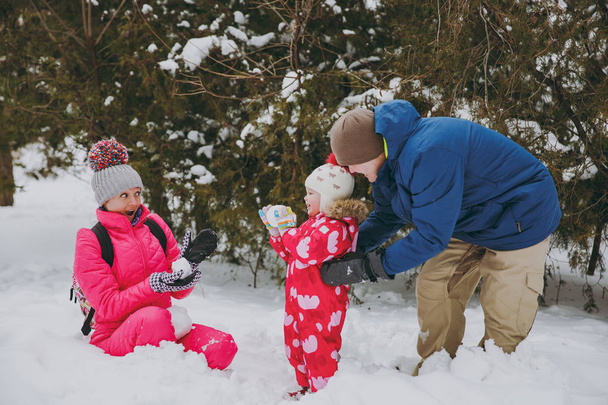 Cheerful family woman, man little girl in winter warm clothes play, make snowballs in snowy park or forest outdoors. Winter fun, leisure on holidays. Love relationship family people lifestyle concept - Photo, Image