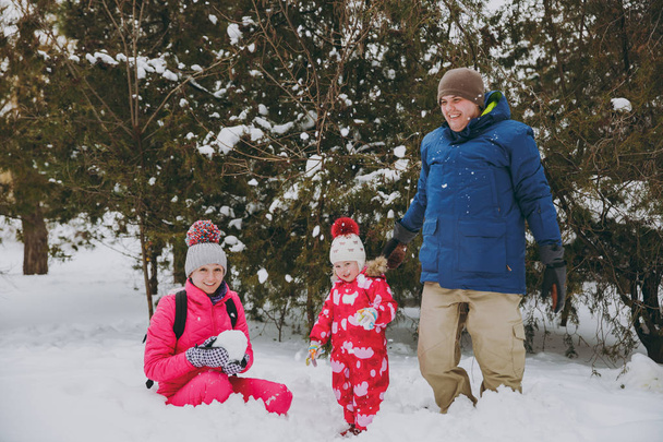 Funny family woman, man and little girl in winter warm clothes play make snowballs in snowy park or forest outdoors. Winter fun, leisure on holidays. Love relationship family people lifestyle concept - Photo, Image