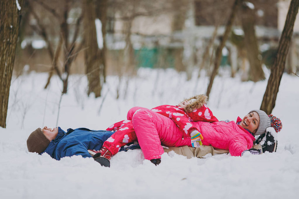 Femme de famille joyeuse, homme petite fille en hiver vêtements chauds couchés sur la neige, écartant les mains dans le parc ou la forêt à l'extérieur. Amusement d'hiver, loisirs en vacances. Amour relation gens style de vie concept
 - Photo, image