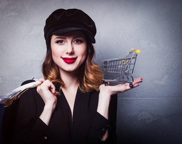 Style redhead girl in hat with shopping bags and cart on grey background - Photo, Image