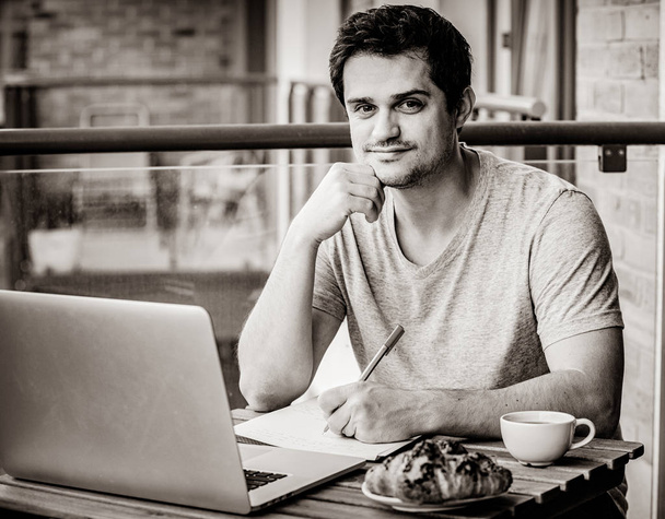 Красивый молодой менеджер, работающий с ноутбуком, сидя дома на улице. Концепция работы со стартапом. Изображение в черно-белом цвете
 - Фото, изображение