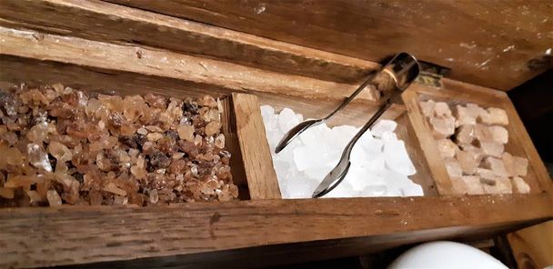 eine Gruppe Steinzucker. braune Zuckerwürfel in Holzkiste. verschiedene Tees und verschiedene Zuckerarten auf Holztisch - Foto, Bild