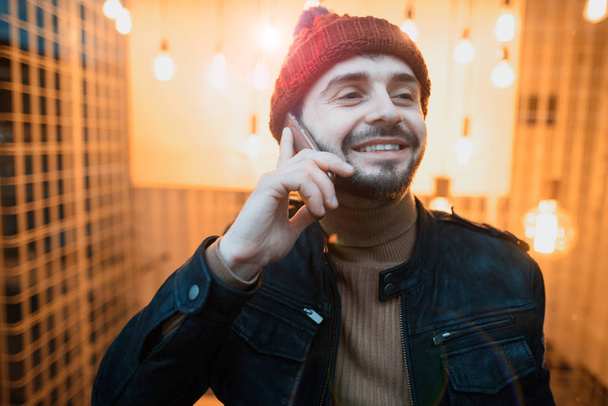 A happy hipster guy talking on a smartphone. Against the background of lamps - Foto, Bild