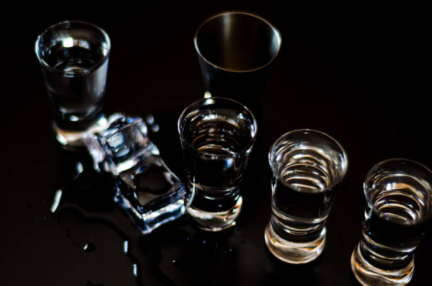 Traditionele zuivere wodka in glazen op een zwarte achtergrond, gekoeld drankje, nachtleven - Foto, afbeelding
