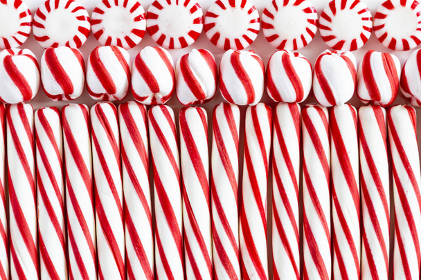 Close up of background of rows of red and white striped peppermint sticks, round mints and swirled candy balls - Фото, изображение