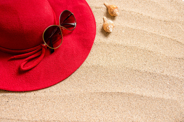 red hat on sandy beach with sunglasses, seashells and copy space for text. - Фото, изображение