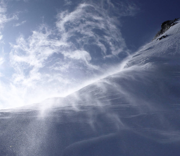 ráfagas de viento tormentoso soplan nieve sobre una cresta de montaña con cielos tormentosos detrás
 - Foto, imagen