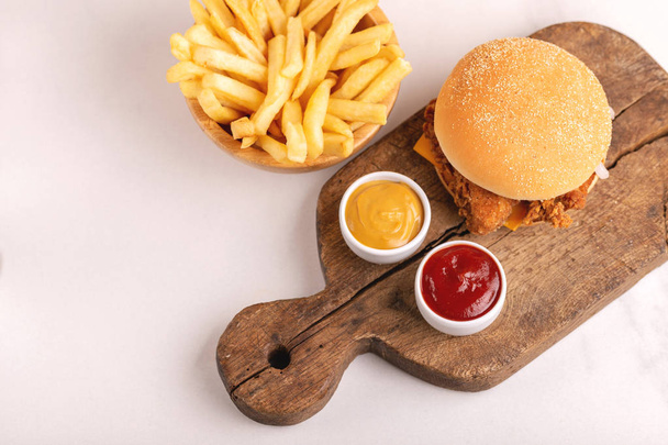 Delicious but unhealthy food with ketchup and mustard on vintage cutting board. Fast carbohydrates, junk and fast food. Light marble background. - 写真・画像