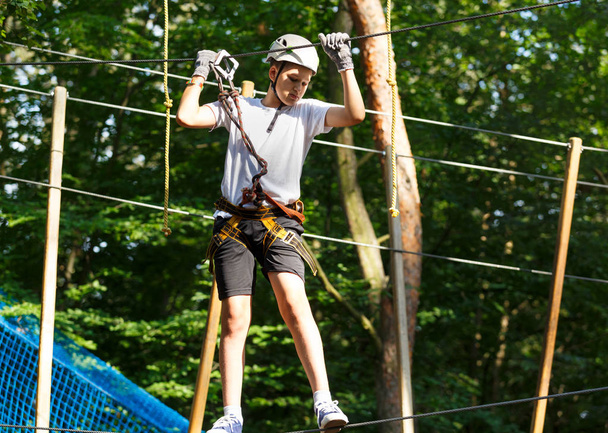 Netter Junge, der an einem sonnigen Sommertag Aktivitäten im Klettererlebnispark genießt. Kinder klettern in Seilspielplatz Struktur. Sicheres Klettern mit Helmversicherung. Kind im Wald-Erlebnispark, Extremsport - Foto, Bild