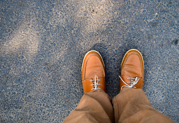 Bu kahverengi deve renkli aksanlı konuşma deri ayakkabı bağlı dantel üst bir görünümdür. Ayakkabı da kahverengi/Haki renkli pantolon veya pantolon giyen bir asfalt yolda duran bir kişi tarafından giyilir - Fotoğraf, Görsel
