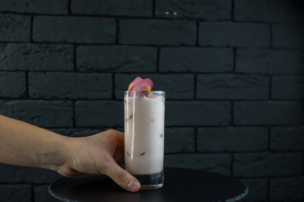 El camarero sirve un cóctel alcohólico lechoso blanco dulce con jugo de fresa con cubitos de hielo, tónico y vodka en una mesa negra en el bar. Bebidas alcohólicas. Vida de club nocturno
 - Foto, imagen