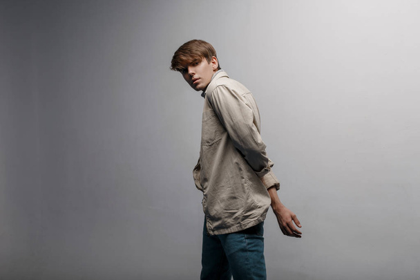 Mladý pohledný muž s módní účes v lehké jarní světlo vintage elegantní sako v módní modré kalhoty, pózuje v studio poblíž bílé zdi. Evropská fešák. Moderní Pánská móda - Fotografie, Obrázek