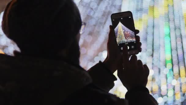 Weergave achterzijde: bebaarde man nemen van foto's van Europese kerst markt scène op smartphone. Close-up video - Video