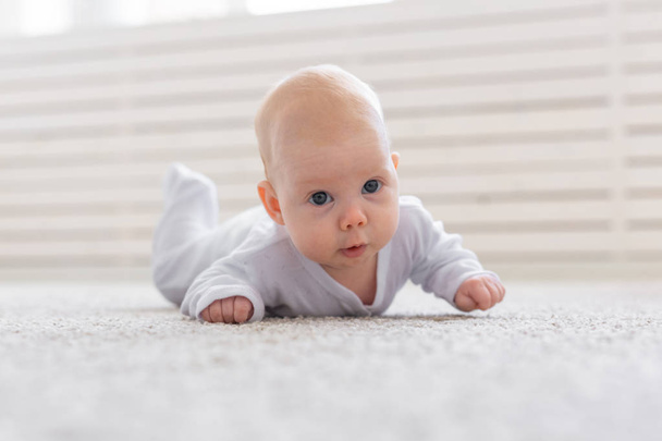 παιδική ηλικία, άνθρωποι και αχρωμικές έννοια - μικρό μωρό αγόρι ή κορίτσι που σέρνεται στο πάτωμα στο σπίτι - Φωτογραφία, εικόνα