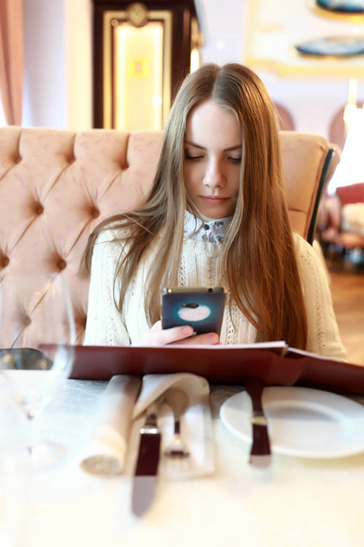 Young woman with menu book and smartphone in restaurant - Photo, Image