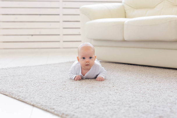 Kindheits-, Baby- und Personenkonzept - kleiner Junge oder Mädchen, die zu Hause auf dem Boden krabbeln - Foto, Bild
