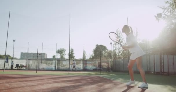 Fiatal szőke haj sportiv nő játszik tenisz profi külső napsütéses napon teniszpálya. - Felvétel, videó