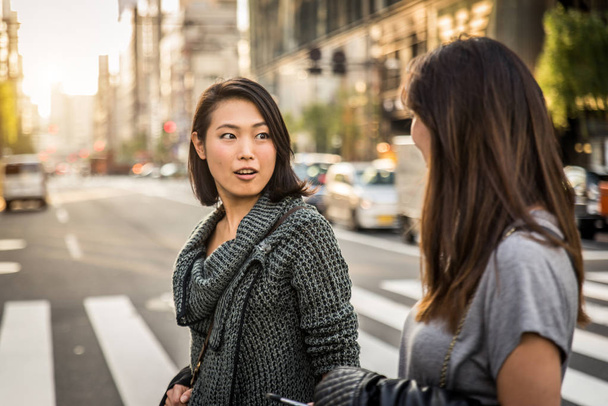 Two girlfriends meeting outdoors and having fun - Japanese people bonding on Tokyo streets - Photo, image
