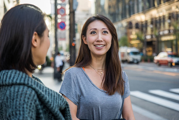 Two girlfriends meeting outdoors and having fun - Japanese people bonding on Tokyo streets - Photo, image