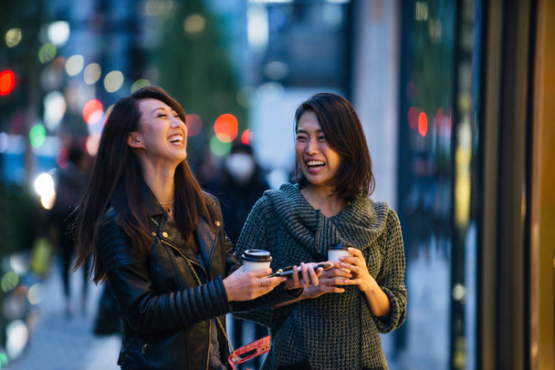 Two girlfriends meeting outdoors and having fun - Japanese people bonding on Tokyo streets - Photo, Image